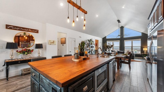 kitchen with an island with sink, wooden counters, hanging light fixtures, stainless steel appliances, and dark wood-type flooring