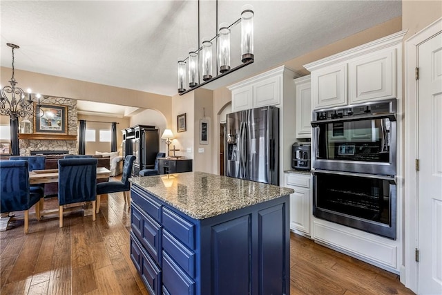 kitchen featuring multiple ovens, decorative light fixtures, white cabinets, stainless steel refrigerator with ice dispenser, and blue cabinetry