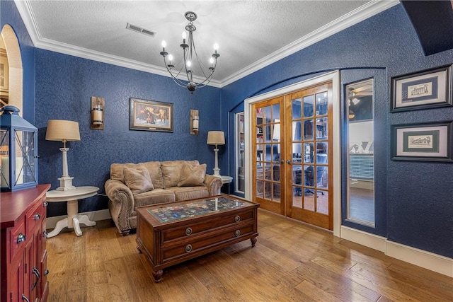 living room with crown molding, hardwood / wood-style floors, an inviting chandelier, and french doors