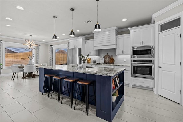 kitchen with pendant lighting, an island with sink, white cabinets, light stone counters, and stainless steel appliances