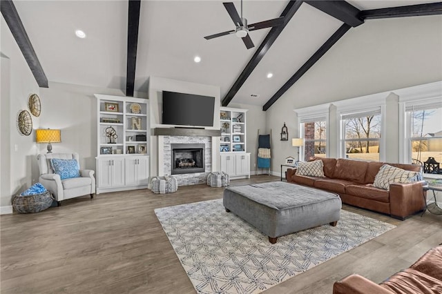 living room featuring a stone fireplace, high vaulted ceiling, light hardwood / wood-style flooring, beamed ceiling, and ceiling fan