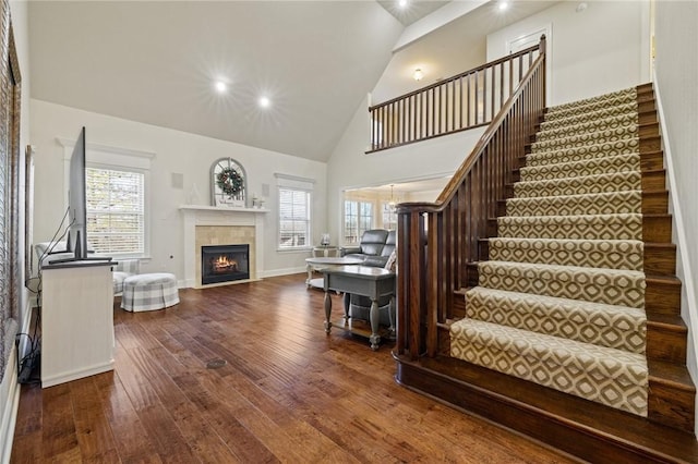 living room featuring a tiled fireplace, wood-type flooring, high vaulted ceiling, and a healthy amount of sunlight