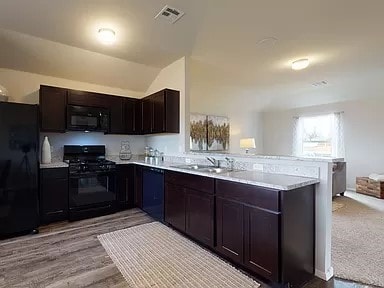 kitchen with black appliances, sink, dark brown cabinetry, kitchen peninsula, and light hardwood / wood-style flooring