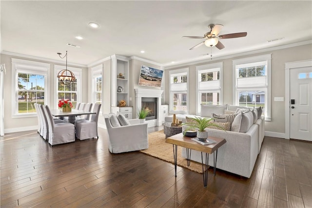 living room featuring dark wood-type flooring, ornamental molding, and ceiling fan with notable chandelier