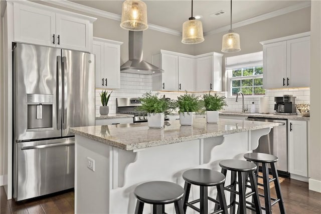 kitchen with decorative light fixtures, white cabinetry, a center island, stainless steel appliances, and wall chimney exhaust hood