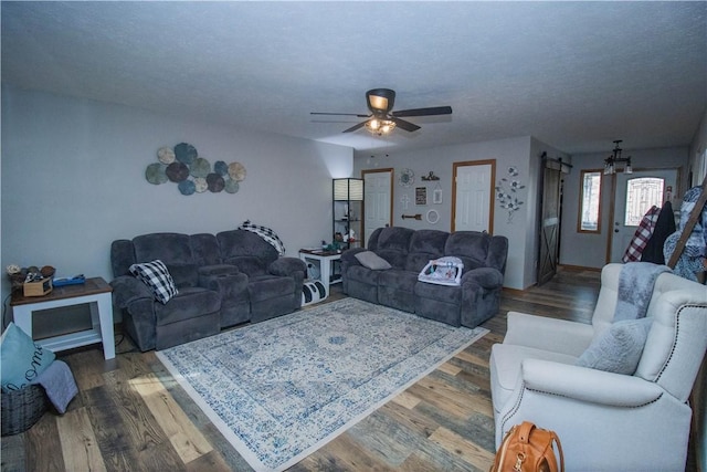 living room featuring ceiling fan, wood-type flooring, a barn door, and a textured ceiling