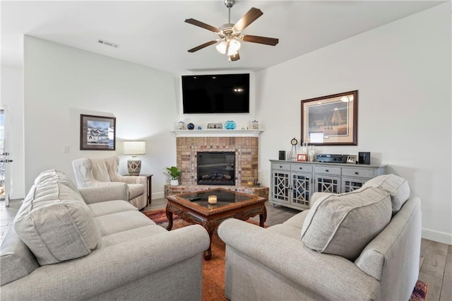 living room featuring ceiling fan, a fireplace, and light wood-type flooring