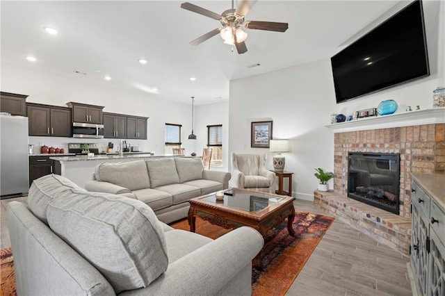 living room with ceiling fan, light hardwood / wood-style floors, and a brick fireplace