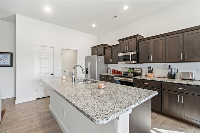 kitchen with stainless steel appliances, a center island with sink, and light stone counters