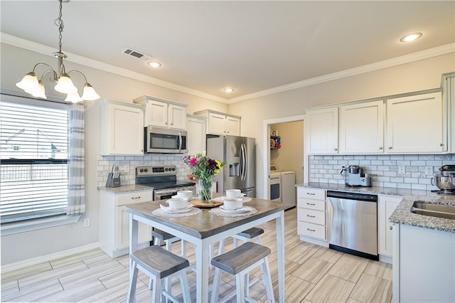 kitchen featuring washer and dryer, white cabinetry, hanging light fixtures, stainless steel appliances, and light stone countertops