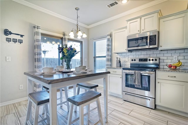 kitchen with pendant lighting, backsplash, stainless steel appliances, light stone countertops, and white cabinets