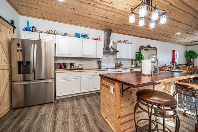 kitchen with stainless steel refrigerator with ice dispenser, wall chimney exhaust hood, gas range gas stove, hanging light fixtures, and white cabinets