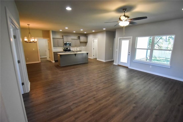 unfurnished living room featuring ceiling fan with notable chandelier, sink, and dark wood-type flooring