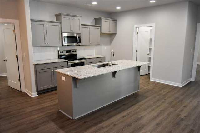 kitchen with appliances with stainless steel finishes, sink, a kitchen bar, light stone countertops, and a center island with sink