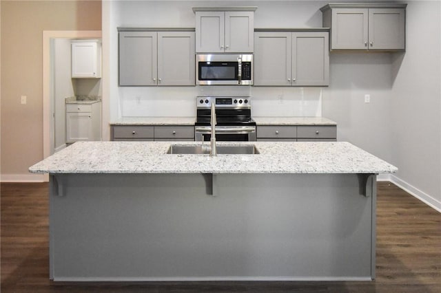 kitchen featuring light stone countertops, gray cabinets, stainless steel appliances, and a center island with sink