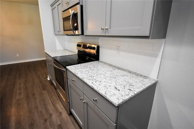 kitchen with gray cabinetry, tasteful backsplash, dark hardwood / wood-style flooring, stainless steel appliances, and light stone countertops