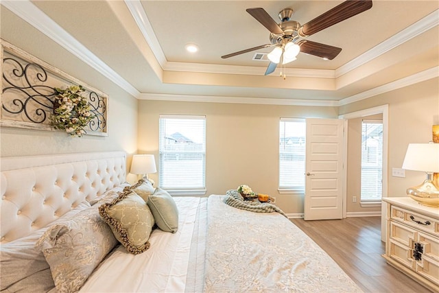 bedroom featuring multiple windows, a tray ceiling, light hardwood / wood-style flooring, and crown molding