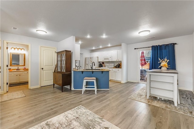 kitchen with sink, light wood-type flooring, white appliances, a kitchen island with sink, and white cabinets