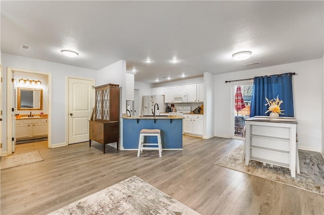 kitchen with sink, white appliances, light hardwood / wood-style flooring, a breakfast bar area, and white cabinets