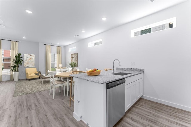 kitchen with a healthy amount of sunlight, stainless steel dishwasher, white cabinets, and light wood-type flooring