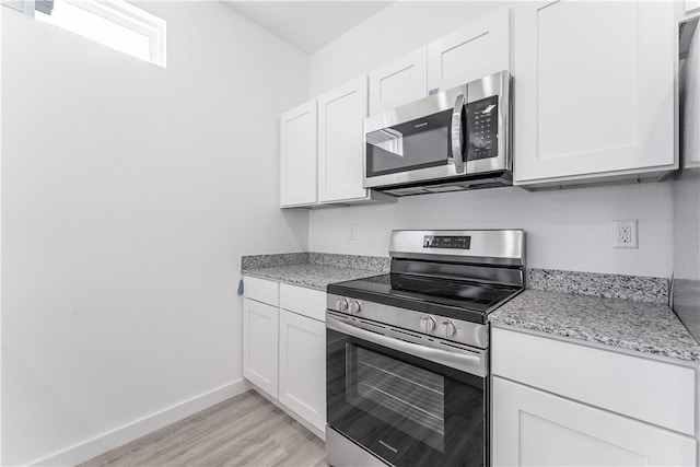 kitchen with white cabinetry, light stone countertops, stainless steel appliances, and light wood-type flooring