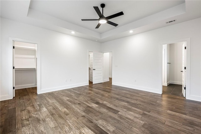 unfurnished bedroom with a raised ceiling, dark hardwood / wood-style floors, connected bathroom, and a spacious closet