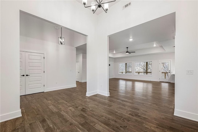 unfurnished living room with dark hardwood / wood-style flooring, a raised ceiling, ceiling fan with notable chandelier, and a high ceiling