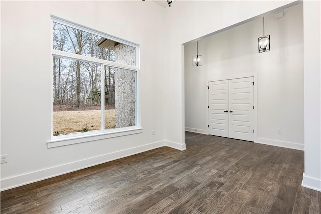 unfurnished dining area featuring a towering ceiling, plenty of natural light, and dark hardwood / wood-style floors