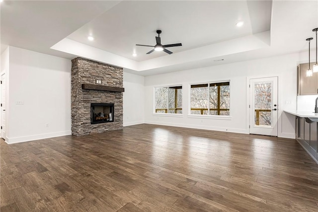 unfurnished living room featuring dark wood-type flooring, ceiling fan, a fireplace, and a raised ceiling