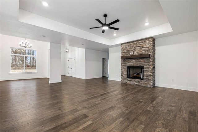 unfurnished living room with dark wood-type flooring, ceiling fan with notable chandelier, a fireplace, and a tray ceiling