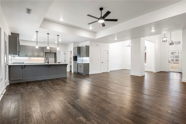 unfurnished living room with a tray ceiling, sink, ceiling fan with notable chandelier, and dark wood-type flooring