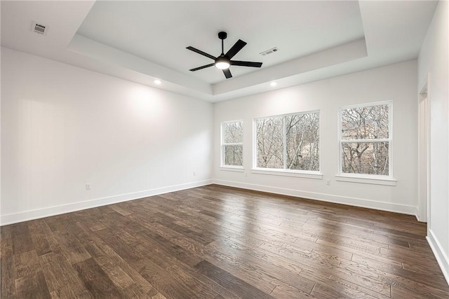 empty room with dark hardwood / wood-style flooring, a raised ceiling, and ceiling fan