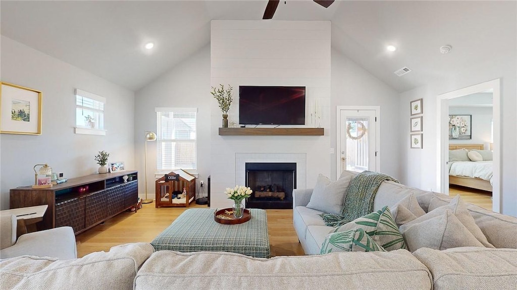 living room with ceiling fan, a large fireplace, high vaulted ceiling, and light wood-type flooring