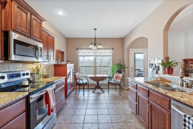 kitchen with sink, hanging light fixtures, light stone counters, stainless steel appliances, and a textured ceiling