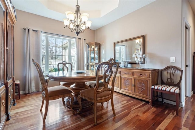 dining space with wood-type flooring, a tray ceiling, and a notable chandelier