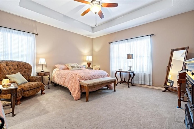 bedroom with light colored carpet, ceiling fan, and a tray ceiling