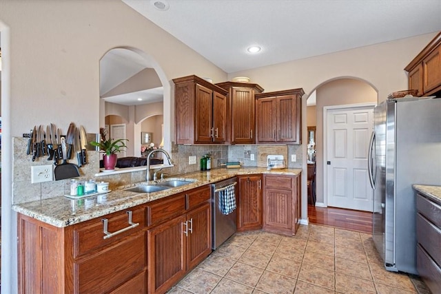 kitchen with tasteful backsplash, appliances with stainless steel finishes, sink, and light stone counters