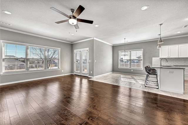 unfurnished living room with ornamental molding, ceiling fan with notable chandelier, a textured ceiling, and dark hardwood / wood-style flooring