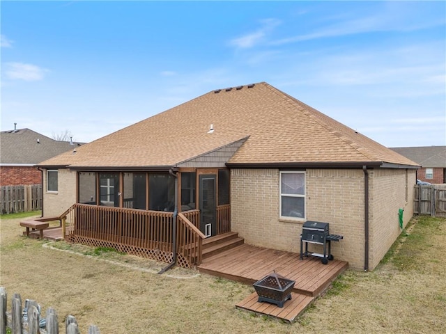 back of property with a wooden deck, a sunroom, a fire pit, and a lawn