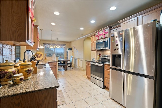 kitchen featuring light tile patterned floors, crown molding, hanging light fixtures, backsplash, and stainless steel appliances