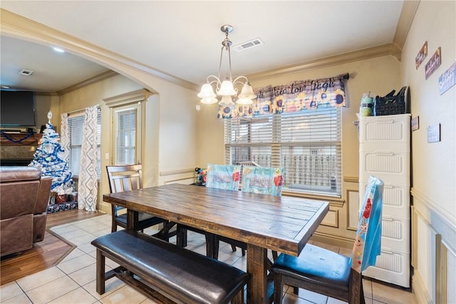 tiled dining room with ornamental molding and a chandelier