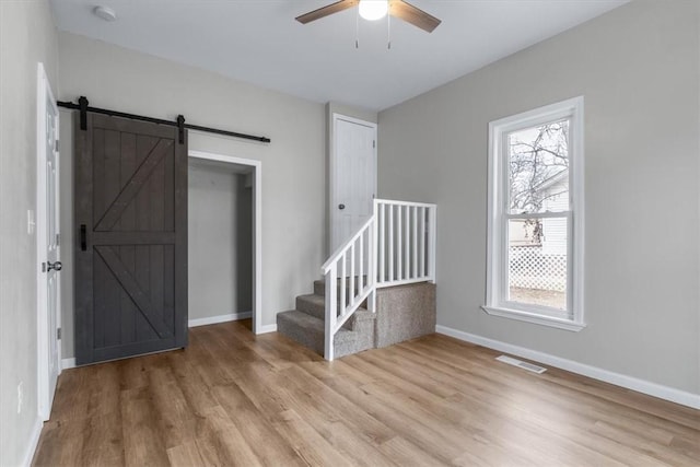 entrance foyer with a barn door, ceiling fan, and light wood-type flooring