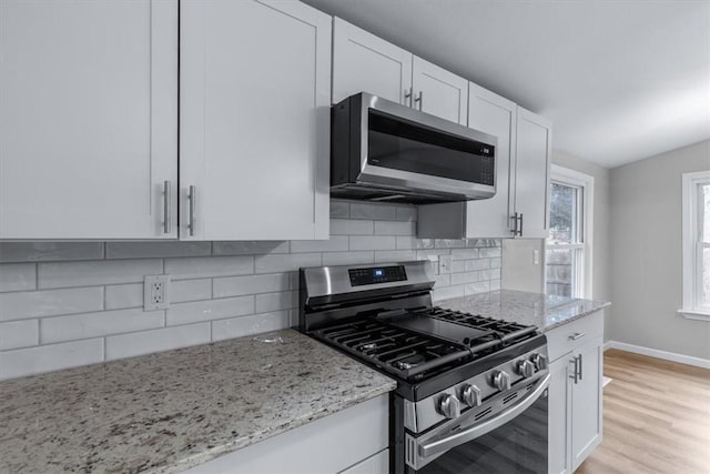 kitchen featuring light stone counters, backsplash, white cabinets, and appliances with stainless steel finishes