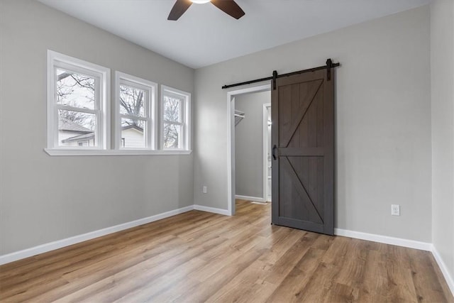 unfurnished bedroom with ceiling fan, a barn door, a walk in closet, a closet, and light wood-type flooring