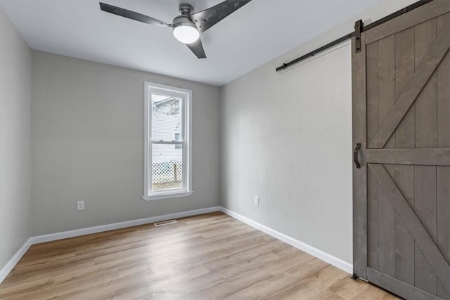 unfurnished room featuring ceiling fan, a barn door, and light wood-type flooring