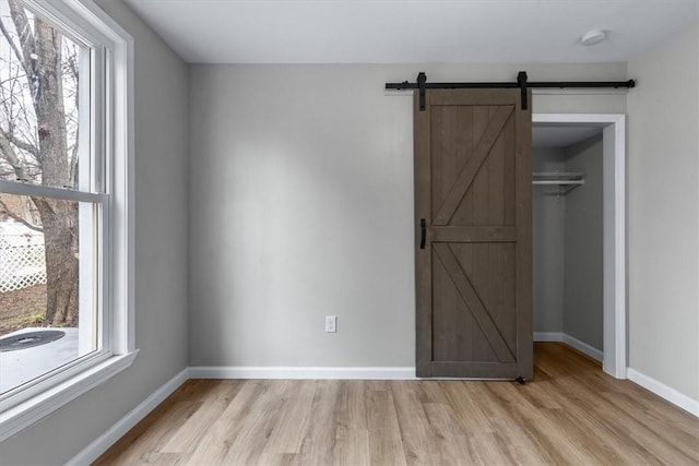 unfurnished bedroom with a closet, light hardwood / wood-style floors, and a barn door