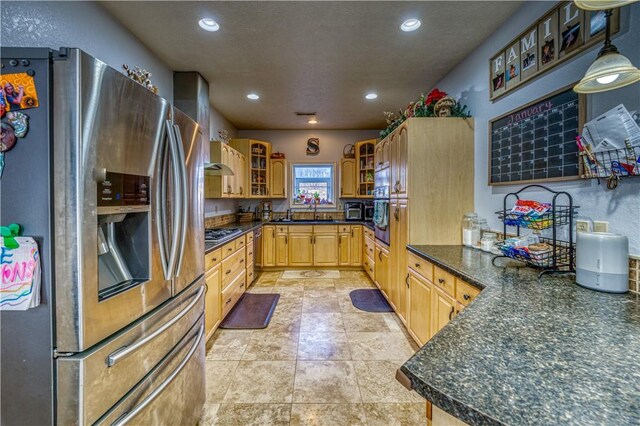 kitchen with appliances with stainless steel finishes, sink, hanging light fixtures, light brown cabinets, and a textured ceiling