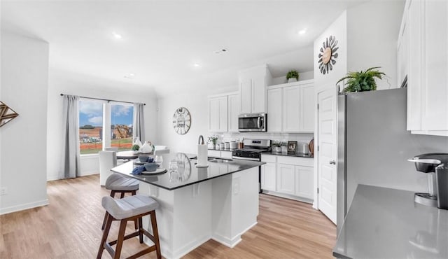 kitchen featuring white cabinetry, appliances with stainless steel finishes, a kitchen breakfast bar, light hardwood / wood-style floors, and backsplash