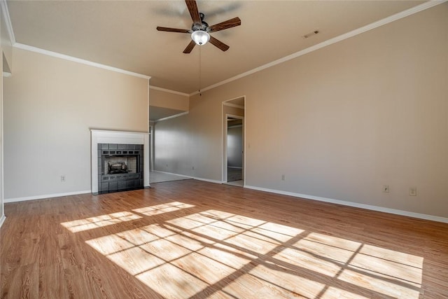 unfurnished living room featuring ceiling fan, wood finished floors, ornamental molding, a tile fireplace, and baseboards