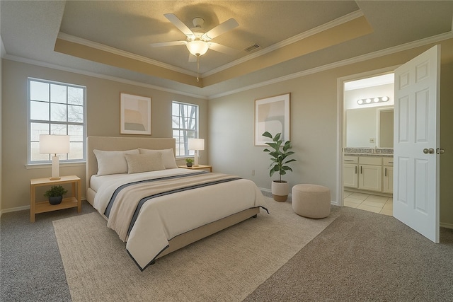 bedroom with a tray ceiling, light carpet, ornamental molding, ensuite bathroom, and baseboards
